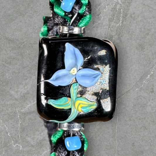 Blue flower on black and green cord with sky blue seed beads